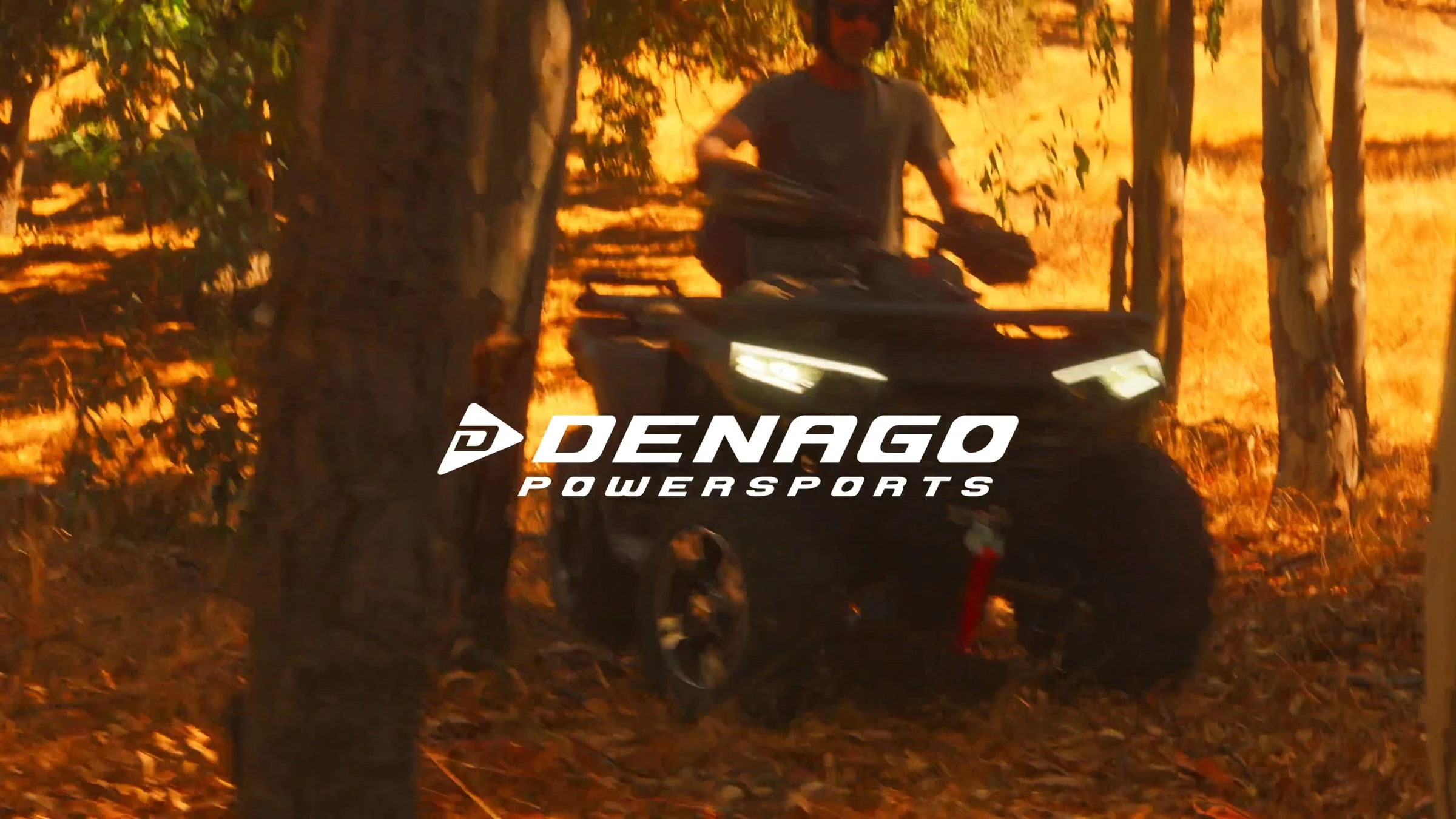 Off-road vehicle driving through wooded terrain with Denago Powersports branding, showcasing outdoor adventure and recreational riding experience in nature.