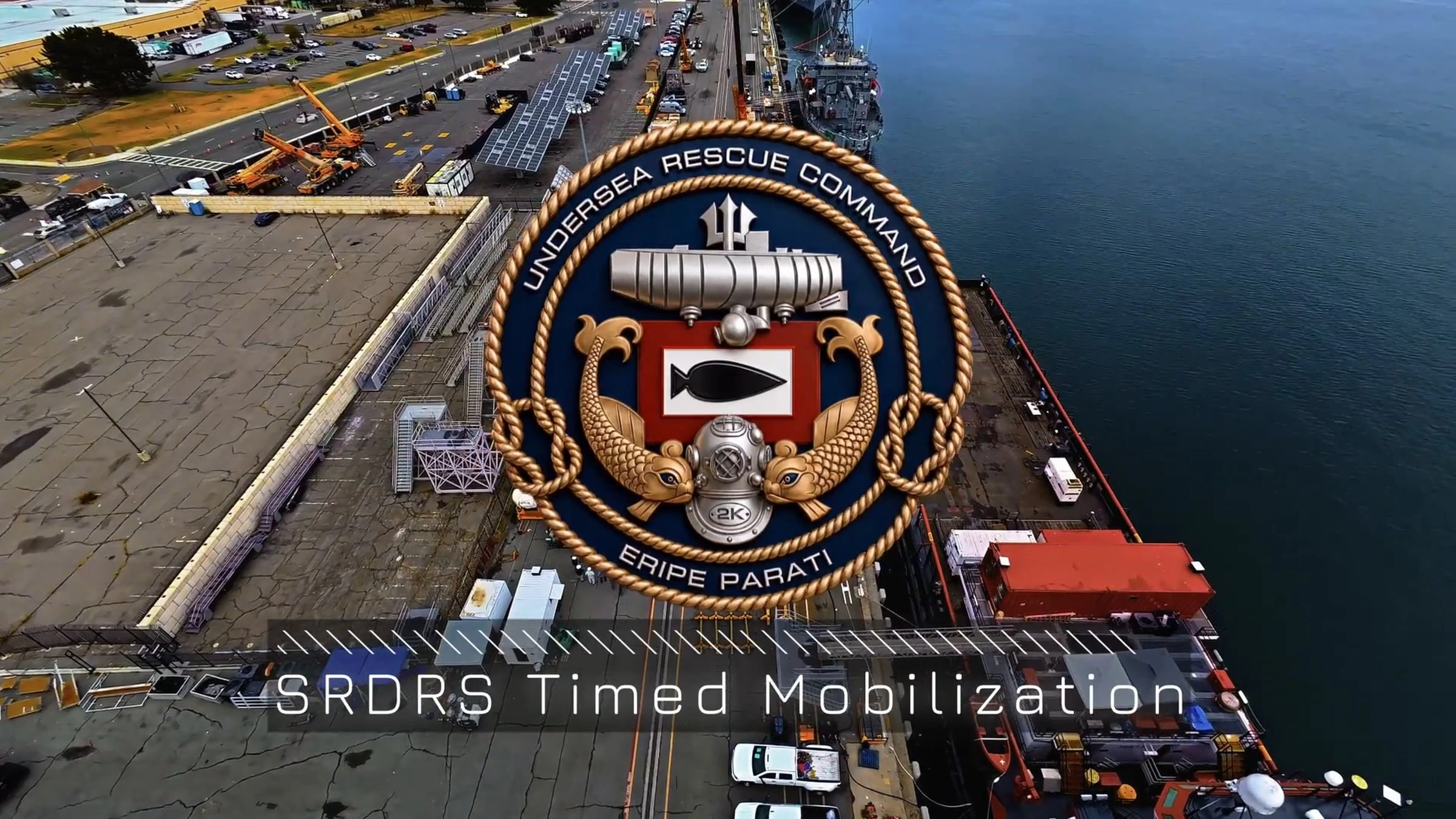 Aerial view of a waterfront industrial port featuring the U.S. Navy Undersea Rescue Command emblem