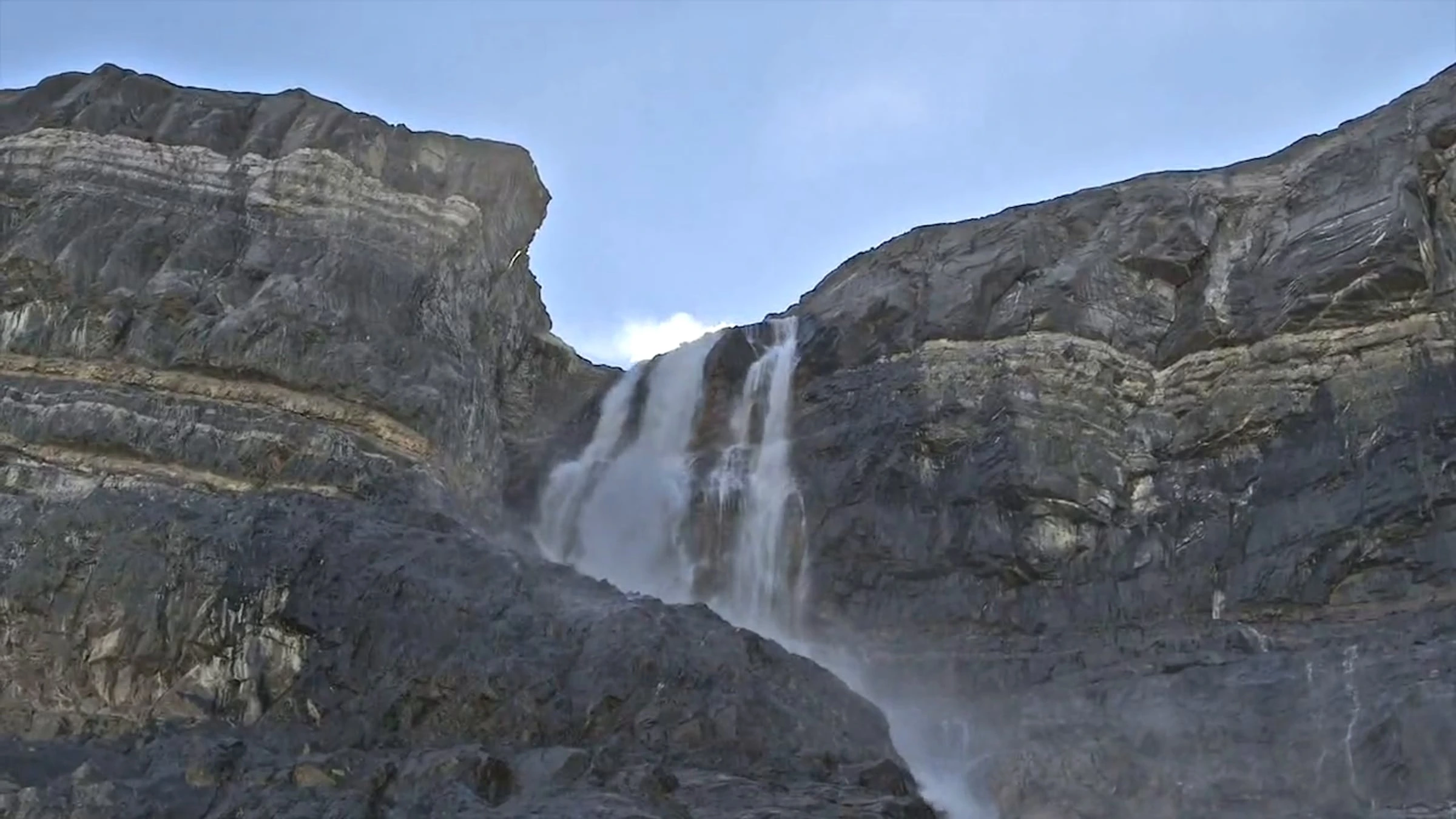 Waterfall flowing between towering rocky mountain cliffs